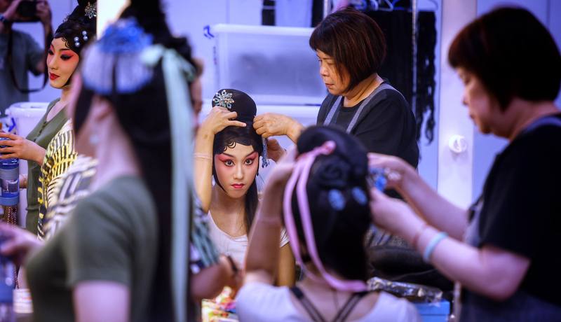 國光劇團箱管組組長、負責包頭容妝的張美芳（右），在京劇旦角演出前，用巧手細心為演員貼上小彎髮片修飾額前，再用大柳鬢勾勒完美臉型