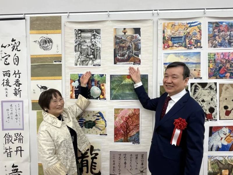 第22屆「美超越國界」國際水墨展於23日在東京國立新美術館開幕，駐日代表李逸洋與促成台灣作品參展推手之一的醫師中山玉惠於台灣展區兒童作品前合影。（文化部駐日台灣文化中心提供）