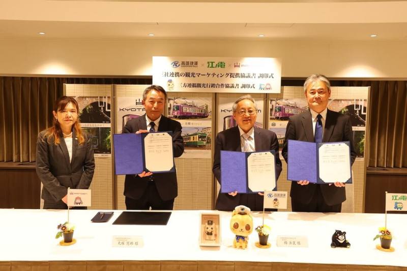 高雄捷運公司「蜜柑站長」行銷至日本，高雄捷運公司董事長楊岳崑（右2）13日與日本嵐電社長大塚憲郎（左2），在江之電取締役露木健勝（右1）、京都右京區長人見早知子（左1）見證下，完成三方合約簽訂。（高捷公司提供）