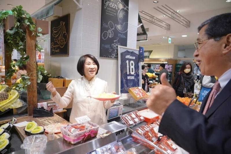 屏東縣長周春米（前左）化身農產行銷大使，7日到日本九州「南國水果岩田屋」本店出席屏東蜜棗暨鳳梨展售會，展售會場日本民眾試吃屏東鳳梨及蜜棗，豎起大拇指比讚。（屏東縣政府提供）