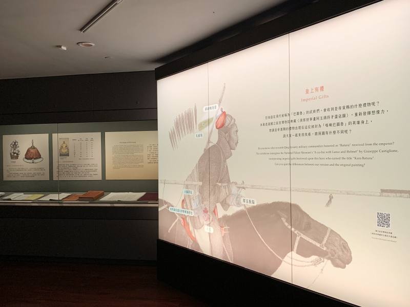 展場燈箱設計讓院藏〈清郎世寧畫阿玉錫持矛盪寇圖〉畫中人物戴上本次展件的翠玉扳指、火鐮荷包展件，讓觀眾具體想像天子的禮物。
