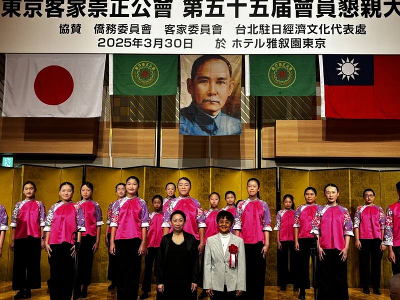 日本具歷史規模的客家僑團「東京崇正公會」30日在東京舉辦第55屆懇親大會，國立客家兒童合唱團在會中獻唱客家歌謠，活潑生動的演出博得滿堂彩。指揮彭孟賢（左）、客委會主委古秀妃與兒童合唱團團員合影。