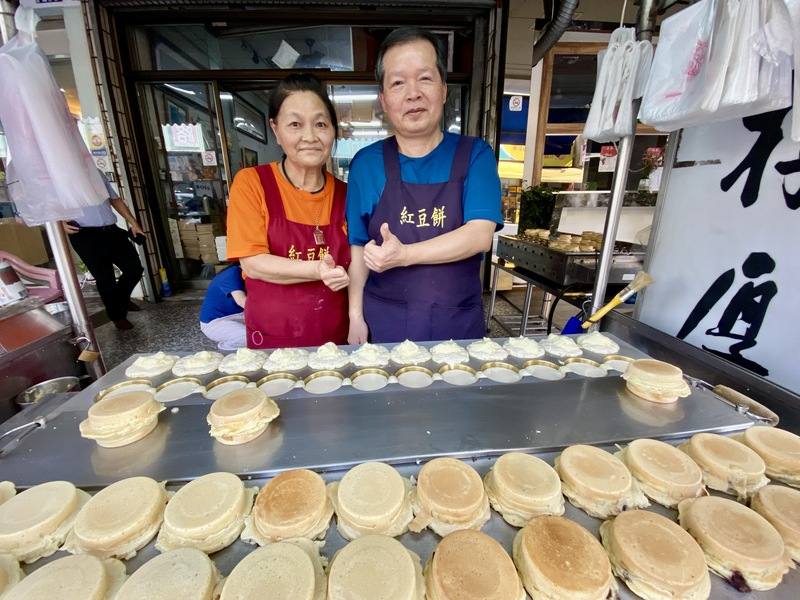 在台中賣紅豆餅的夫妻黃啟晏（右）、賴双鳳（左）是交通志工的一員，21年來不分寒暑，每天早上站在街頭為孩童指引交通，成為學校最美風景