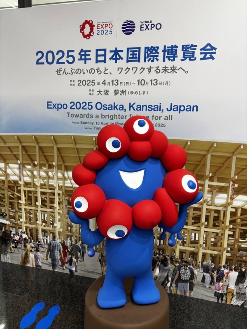 到大阪世博會場的參觀民眾，第一件事都是和吉祥物「脈脈」合影打卡。儘管這個紅藍相間的吉祥物剛推出時被批評為「外型獵奇」，但現在已經成為世博不可或缺的門面角色。圖為車站內為大阪世博宣傳的「脈脈」