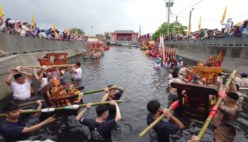 嘉義縣布袋鎮新塭嘉應廟24日舉辦「衝水路、迎客王」活動，轎班以雙手將神轎舉高，衝入新塭國小西側王爺窟（王船碼頭），在感應客王降臨後，逐一上岸起駕回鑾