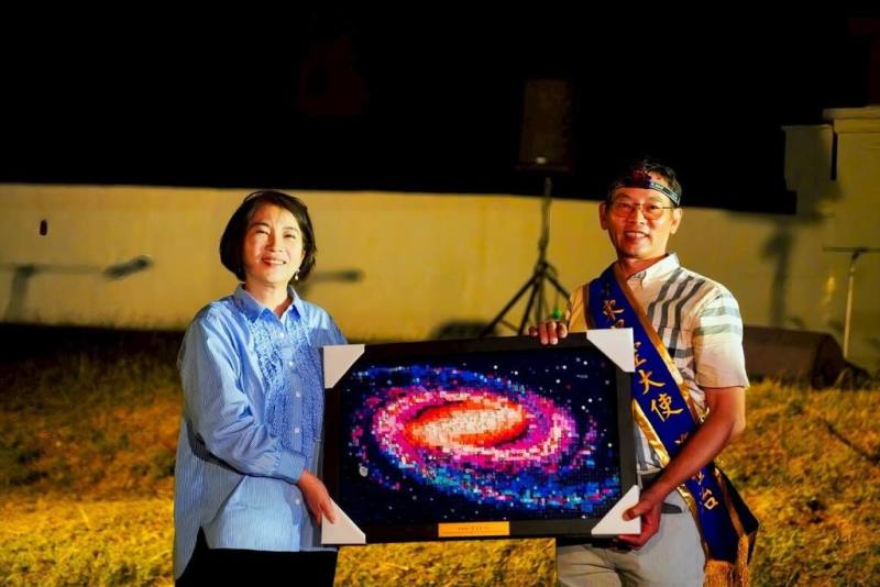 屏東縣政府連4個週末舉辦「來恆春擁抱宇宙」活動，星空大使施世治（右）協助向民眾解說星空知識，屏東縣長周春米（左）特別致贈星空積木圖，感謝他對推廣天文教育熱情與付出。（屏東縣政府傳播暨國際事務處提供）
