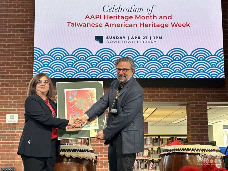 密西根人文協會楊逸鴻博士(左)代表國立臺灣美術館捐贈16幅福蛇版印年畫給安娜堡市立圖書館，由館長艾利‧紐伯格(Eli Neiburger)(右)代表接受。