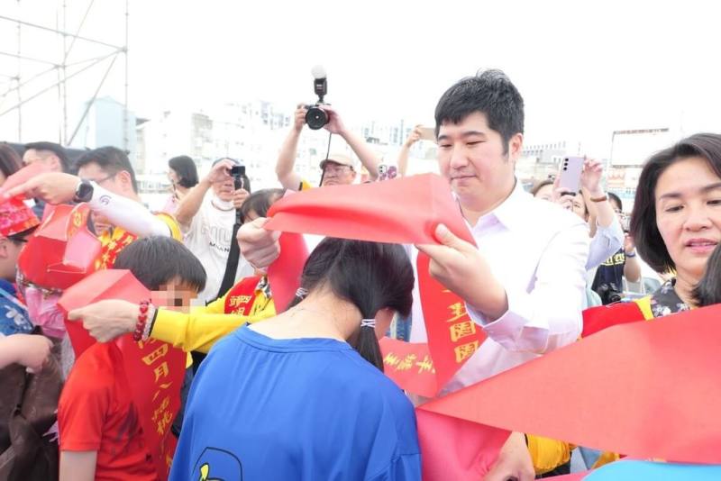 「2025頭份四月八 頭份藝神趣」青年爐主創意供桌迎媽祖競賽5日舉行，客家委員會副主任委員邱星崴（前右白衣者）出席活動，為青年爐主披上紅肩帶，盼這項客庄傳統節慶能持續傳承。（客委會提供）