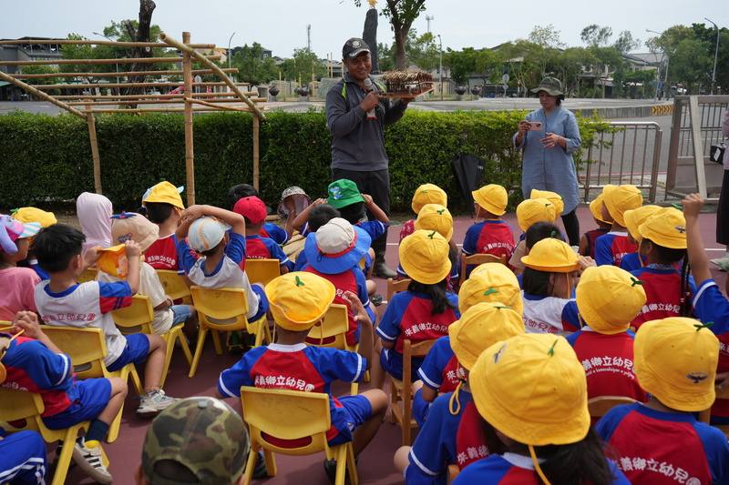 屏東縣來義鄉傳統狩獵文化協會2025年攜手來義鄉立幼兒園，在園內開課，帶領學童認識野生動物及生態環境，了解排灣族如何與山林共存。圖為協會文化講師江人頡（後中）向孩子們解說獵寮功能