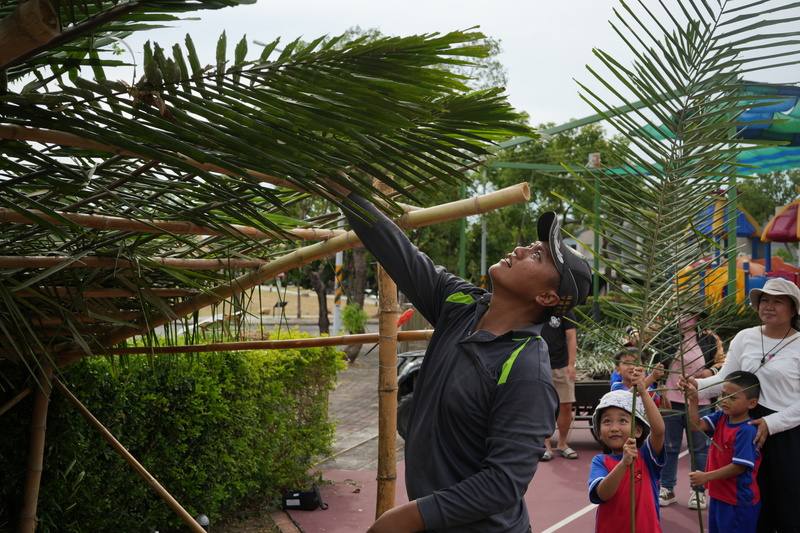 屏東縣來義鄉立幼兒園進行狩獵文化相關課程，由來義鄉傳統狩獵協會文化講師江人頡（左）示範如何搭建獵寮，學童在旁幫忙遞上建材參與