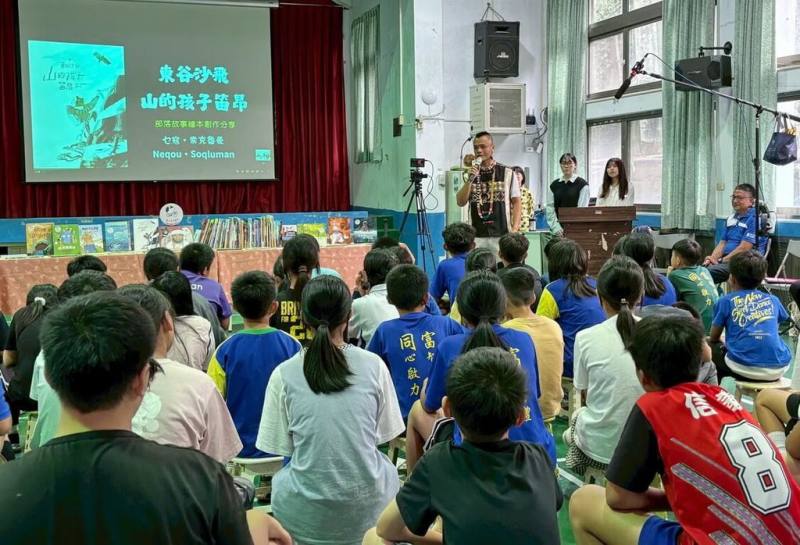 國立台灣圖書館9日邀請布農族作家乜寇．索克魯曼（後持麥克風者）到南投縣信義鄉同富國小與學童分享新作，引導學生從部落語境認識自然、文化。（國台圖提供）