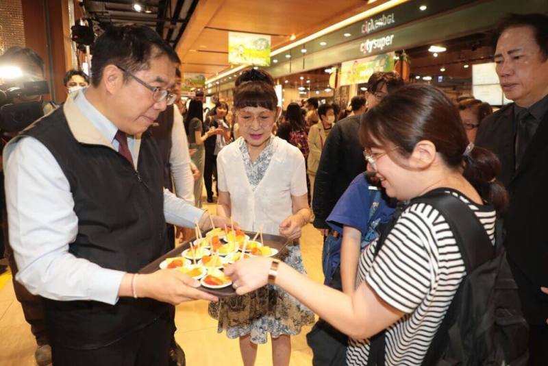 台南市金鑽鳳梨、木瓜與洋香瓜等農產水果，即日起在北台灣8家遠東City Super分店上架銷售。圖為台南市長黃偉哲（前左）14日在新北市板橋大遠百端送水果供民眾試吃。（台南市政府提供）
