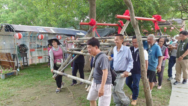 嘉義新港板頭社區發起「地球花園行動」，要打造多處特色景點吸引人潮，16日啟動「蓮花池竹橋茅屋」協力造屋計畫，眾人一同將竹橋底座抬至要搭建竹橋茅屋的蓮花池畔。