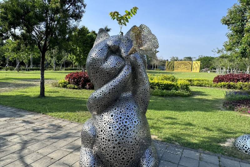 台南山上花園水道博物館入口廣場處的貓造型裝置藝術「幸福．召喚」，因作品中心鏤空，近日館方發現有一株植物從基座下方生長後，穿過作品從頭頂長出枝葉，有遊客覺得像動畫「龍貓」經典撐傘畫面。（館方提供）