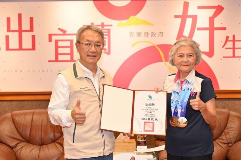 有「噴射機阿嬤」美譽的88歲林潘秀雲（右），曾因韌帶傷勢幾乎無法行走，她選擇靠運動復健，經歷3年努力重返跑道，在2025雙北世壯運拿下4面金牌，宜蘭縣代理縣長林茂盛（左）26日接見表揚。（宜蘭縣政府提供）
