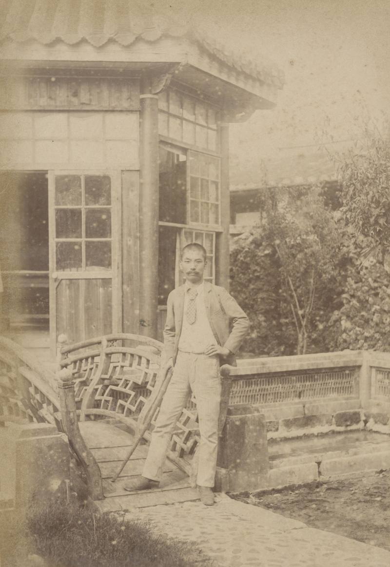 今村巳之助__照片中人物為今村巳之助。拍攝的地點應為日治初期轉為總督府辦公廳舍使用之前清欽差行臺內庭園。照片中顯示庭園的行徑步道鋪有鵝卵石，曲橋的木造欄杆造型亦十分精緻典雅。