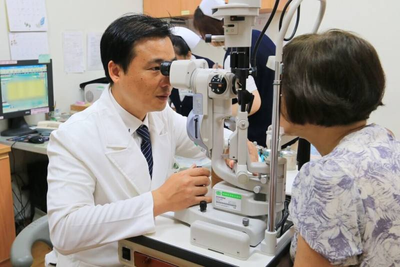 53歲張女士左眼黃斑部裂孔，經3次手術仍未癒合，花蓮慈濟醫院眼科部視網膜科主任何明山（左）檢查發現為極罕見的雙裂孔，採創新雙重療法治療，以羊膜移植修補破洞，並輔以自體高濃度血小板血漿（platelet-rich plasma，PRP）注射，促進組織修復與裂孔癒合。（花蓮慈濟醫院提供）
