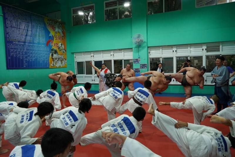 來自日本相撲協會的錣山部屋力士9日下午到訪屏東縣泰武鄉武潭國小，帶領柔道隊學生體驗賽前準備動作，例如輪流抬高左右腿，再用力踏地的「四股」。（屏東縣政府傳播暨國際事務處提供）