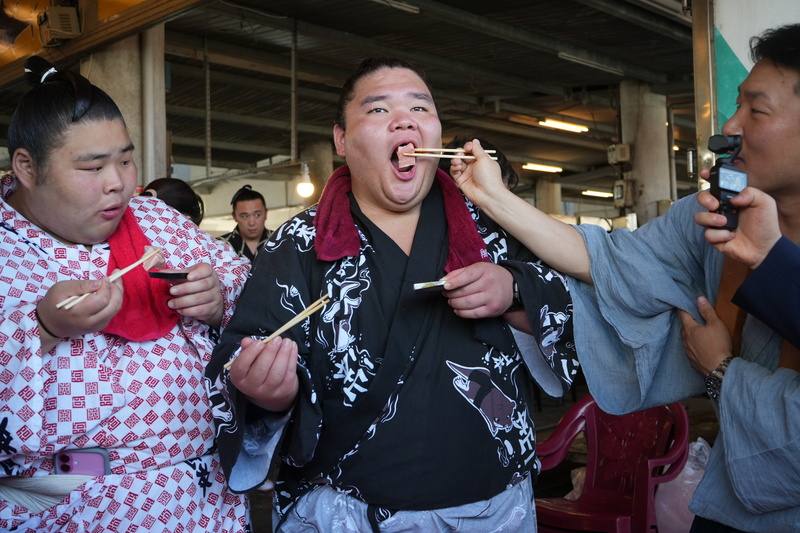 Sumo wrestlers in traditional Japanese garb enjoy raw fish slices at a seafood market by Donggang Fishery Port in Pingtung County Monday. CNA photo June 9, 2025