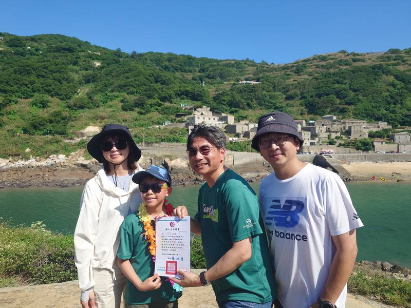 連江縣立中山國中、塘岐國小畢業生需完成鐵人三項後，登上龜島領取畢業證書，塘岐國小畢業生王熙評（左2）完成挑戰領取證書，與校長陳功德（右2）及父母開心合影留念。