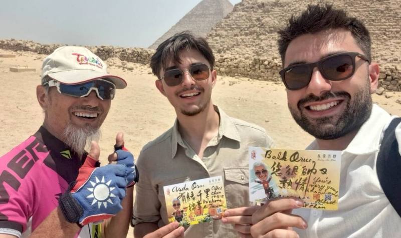 台灣單車不老騎士陳敏先（左）出國總不忘宣傳台灣，將推行國民外交視為志業。圖為陳敏先在金字塔前與相遇的當地人交流，並贈送自己當場揮毫的祝福卡給對方。（陳敏先提供）