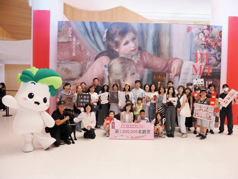 故宮余佩瑾副院長與吉祥物小翠、國寶犬一同於第二展覽館「從印象派到現代主義─美國大都會博物館名作展」入口迎接第999,995名至第1,000,005名共11位觀眾，合影留念並致贈紀念品