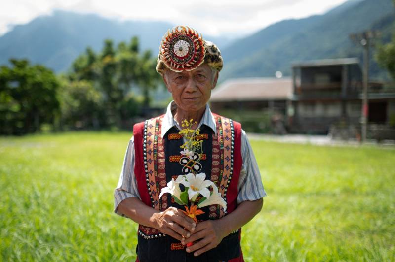 魯凱族耆老包達夫手持部落中象徵最高榮譽的百合花頭飾，他在部落中備受尊崇，被稱為「獵王」，代表其高超的狩獵技藝、豐富的山林智慧與對傳統文化的深刻體現。（攝影／林彥廷／報導者提供）