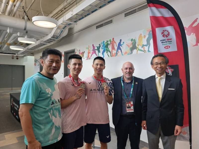 李芳任、李芳至雙胞胎兄弟檔在加拿大羽球公開賽男雙摘金。駐多倫多辦事處長梁毅鵬（右1）與賽事主辦方加拿大羽球協會會長梅瑞特（右2）在賽後向他們及其教練李松遠（左1）致賀。（駐多倫多辦事處提供）