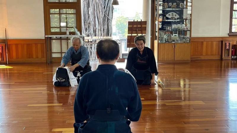 新一集公視台語台文學走讀節目「文學跳曼波」8日晚間播出，作家吳錦發（後排左）特別與武德殿日本劍聖宮本武藏第11代宗家（傳人）陳信寰（背對者）交流劍道，並以「劍道讀心」比喻寫作，認為劍道要讀對手的心，文學就是讀讀者的心。圖右為節目主持人柯大堡