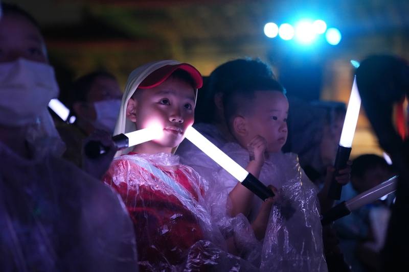 紙風車劇團19日晚間在台北兩廳院藝文廣場舉辦2025客家親子劇「燈怪」首演，由於天候不佳，小朋友穿起雨衣，舉著螢光棒專注看戲