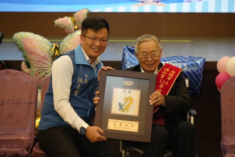 南投縣南投市福山里83歲施大勇（右）曾任茶農、服務於台電，致力推廣龍獅技藝並關注長者福利，為文化推手與社區楷模，今年並獲選南投市公所模範父親，2日由市長張嘉哲（左）表揚。（南投市公所提供）