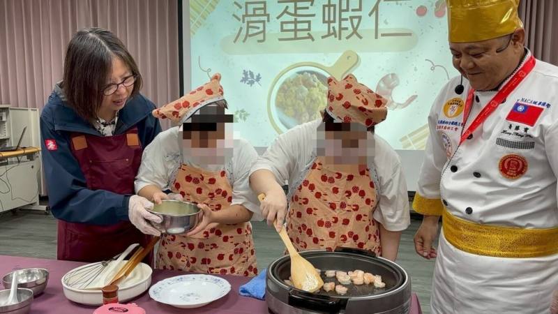 高雄市社會局7日在無障礙之家舉辦「大主廚小跟班的幸福食光」活動，邀請5名憨兒化身小幫手，在主廚黃勝賓（右）指導下，與社會局長蔡宛芬（左）一同烹調料理。（高雄市社會局提供）