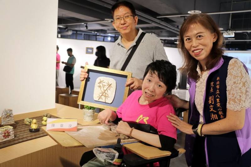 新北市立八里愛心教養院7日在滬尾藝文休閒園區推出特展「陶藝．淘意」，腦麻院生陳韋汝（右2）親手捏製的作品「陶竹」也在站出之列，她開心與教養院長劉文湘（右）及創作作品合影留念。（新北市社會局提供）