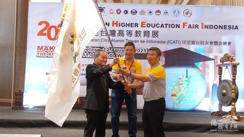 滿任會長林隆雄（左）將會旗交給新任會長梁英民（右），印尼留臺聯總總會長劉俊逸（中）監交