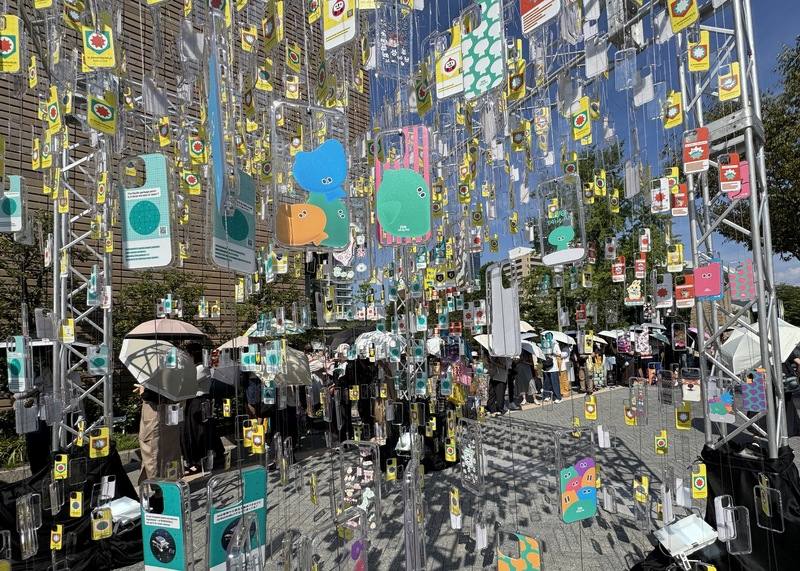 文總主辦的「TAIWAN PLUS 2025 台日新風」邁入第二週，因有許多台灣經典美食攤位，大阪中之島公園湧入人潮。許多人為了購買美食或吉祥物a-We頂著體感溫度攝氏35度高溫撐傘大排長龍