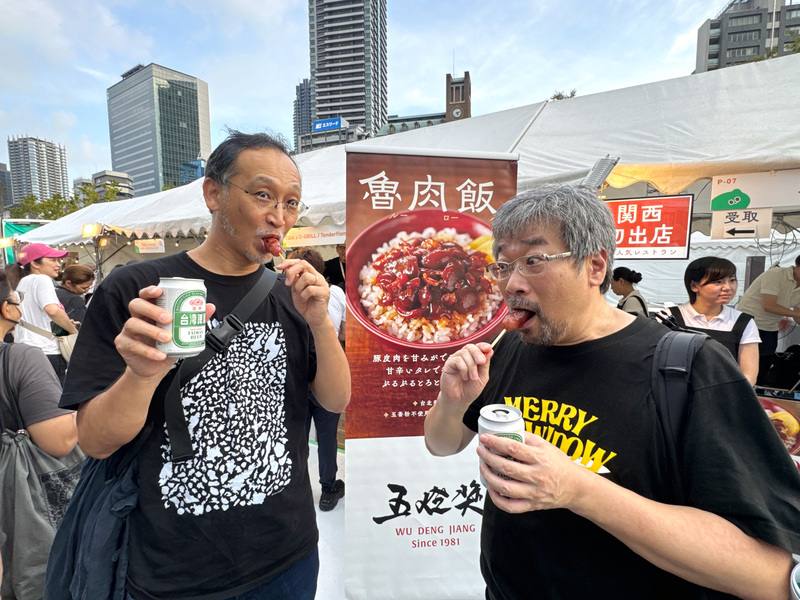 Two Japanese visitors try Taiwanese sausage and beer on Sunday. CNA photo Aug. 17, 2025