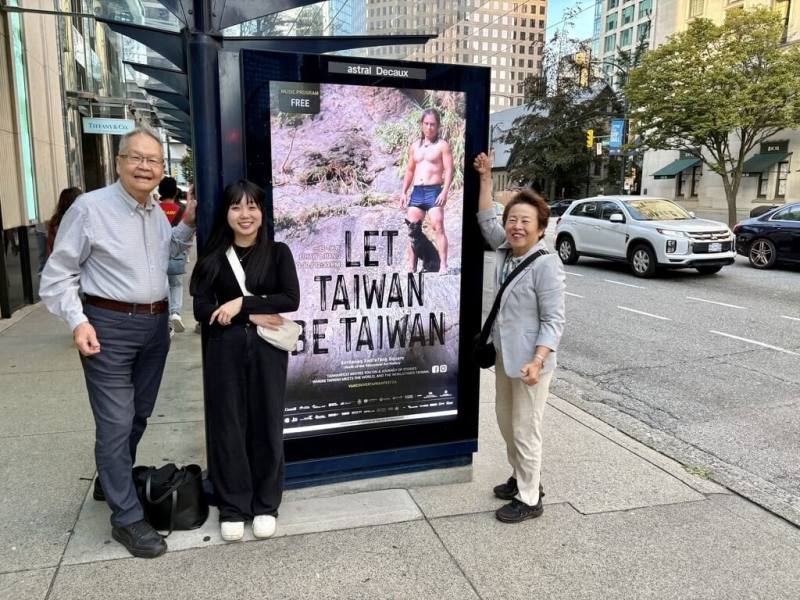 行政院顧問張理瑲（右）和夫婿潘立中（左）很開心和街頭上的「Let Taiwan Be Taiwan」燈箱廣告合影，一名來自日本的年輕女孩（中）還主動加入他們的行列，稱她非常喜觀台灣。（張理瑲提供）