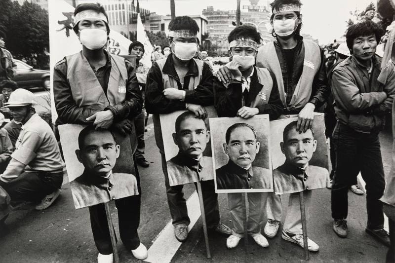 〈還我客家語遊行〉1988年，立法院前。本作品為1988年客家族群發起還我客語運動遊行，遊行隊伍行至立法院前，要求立法還予客家族群權益。畫面中客家族群帶著孫文肖像，強調國父亦為客家人，應尊重國父的母語文化