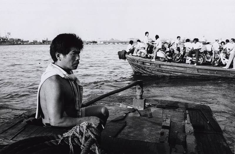 《走拍臺灣》04︰〈高雄旗津〉1987年，旗津舢舨船上。旗津原為高雄市西南部的沙洲半島，與鼓山、前鎮、小港等地隔高雄港相望。1967年為興建高雄港第二港口，截斷與臺灣本島相連處而形成島。1981年始興建過港隧道，1984年完工。由於過港隧道兩端均不在市區，居民長年以來，均以渡輪或舢舨船通勤往返旗津與鼓山之間