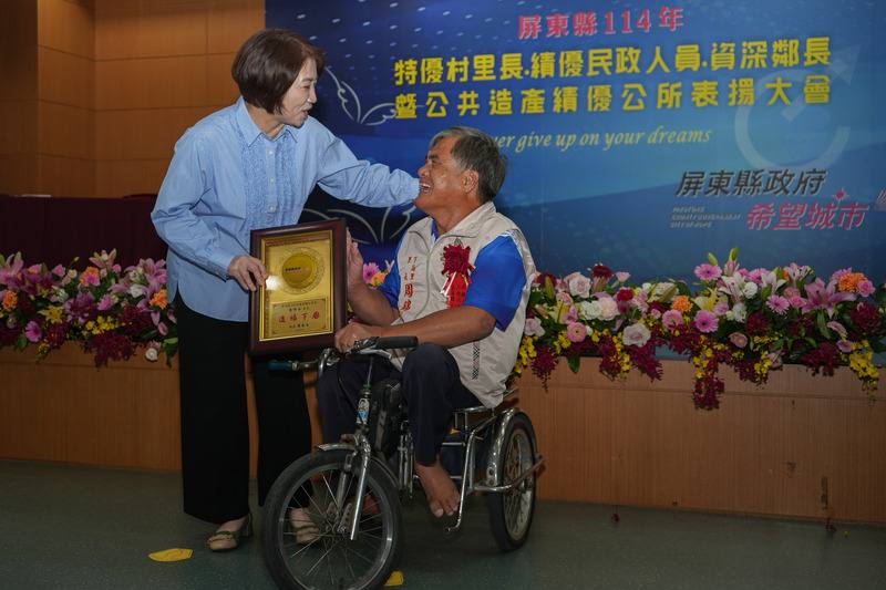 屏東縣政府12日表揚年度特優村里長，東港鎮下廍里長周錦谷（右）雖為身障人士，仍騎特製行動車服務里民，立下身障不設限榜樣，縣長周春米（左）頒發獎牌