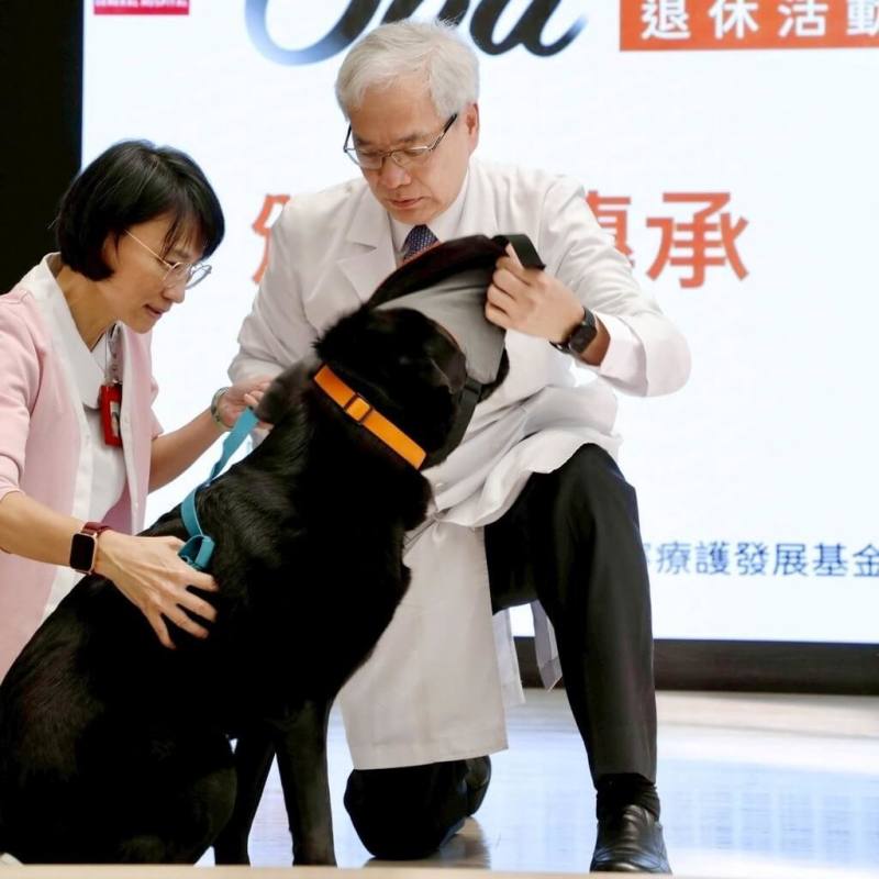 全台首隻駐點醫院的輔助治療犬「歐巴」（黑犬）16日在北榮院長陳威明（右）見證下正式退休，在典禮上卸下專屬服務背心。（北榮提供）