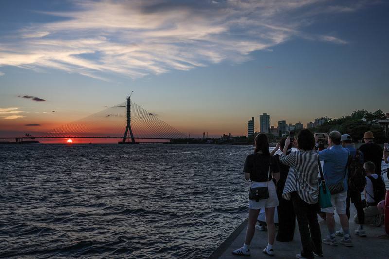 淡江大橋即將在115年通車，外界憂心會擋到淡水的夕陽美景。交通部公路局17日表示，當時會選擇單塔不對稱斜張橋的橋型設計，就是考量淡水夕照可以跟淡江大橋完美融合。圖為民眾傍晚在河岸邊捕捉淡江大橋與夕陽餘暉相互輝映的美景