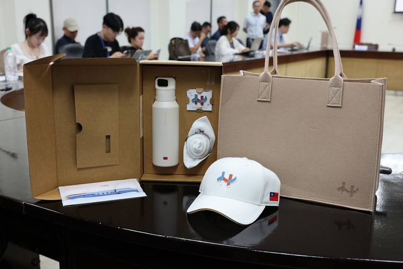 國慶籌備委員會18日展示114年國慶禮賓紀念品，除了棒球帽外，首創以禮盒將徽章、保溫瓶、方巾及口罩搭配呈現，還特別將毛巾摺成玫瑰花
