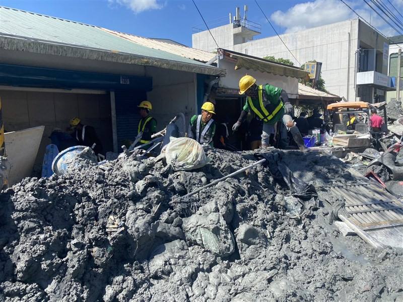 Migrant workers work to remove a thick layer of mud from a street in Guangfu Township, Hualien County Sunday. Photo courtesy of Welldoer House