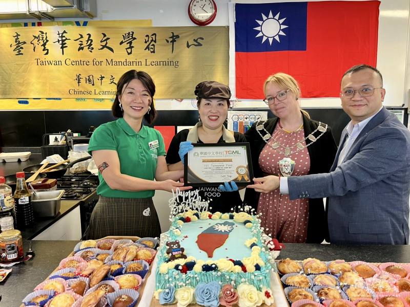 (由左至右)華園中文學校校長曾芳嫻、肯特伯雷郡長史蒂・朱普（Steph Jupe）、駐英國代表處僑務組長葉帝余及「101 Taiwanese Food」餐車大廚 Amanda 與由僑胞郁蘭特製的臺灣生日蛋糕合影，共祝臺灣生日快樂