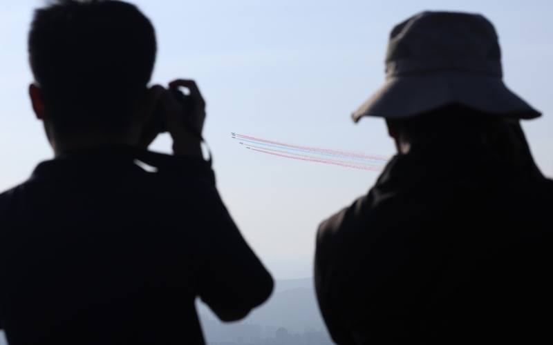 國軍8日清晨進行空中全兵力預演，空軍雷虎特技小組壓軸衝場，5架勇鷹高教機飛過台北市區上空施放彩煙，民眾一早也在觀機平台卡位，用相機捕捉畫面。