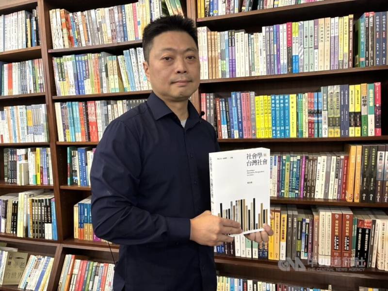 麗文總經理楊宏文拿著旗下品牌巨流出版的「社會學與台灣社會」，為台灣社會學系學生必讀書目，至今已出到第5版，他身後則是擺滿麗文出版品的書牆