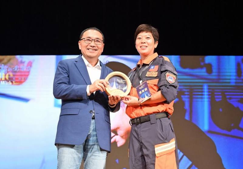新北市政府1日舉辦2025新北影響力「城市共感x創藝漫談」分享會，並表揚10名影響力人物。新北市長侯友宜（左）出席並頒發獎座給入選影響力人物的消防局特搜大隊領犬員羅浩芳（右）。（新北市新聞局提供）