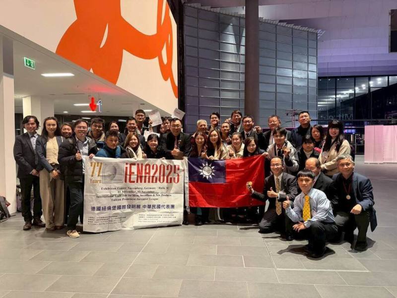 2025年第77屆德國紐倫堡國際發明展（iENA）3日於德國紐倫堡舉行頒獎典禮，台灣代表團以29件作品勇奪26面獎牌，展現創新研發實力。圖為代表團合影，手持國旗與展覽布條合照。（沈毓豪提供）