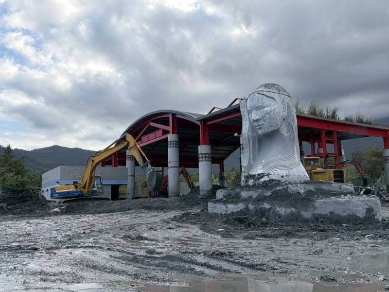 颱風鳳凰帶來風雨造成馬太鞍溪堰塞湖溢流，花蓮萬榮鄉明利部落的精神象徵「紋面阿嬤」雕像也被滾滾而下的土石淹沒；花蓮縣政府團隊動員重型機具連2天不停趕工清淤，讓雕像重現。（花蓮縣政府提供）